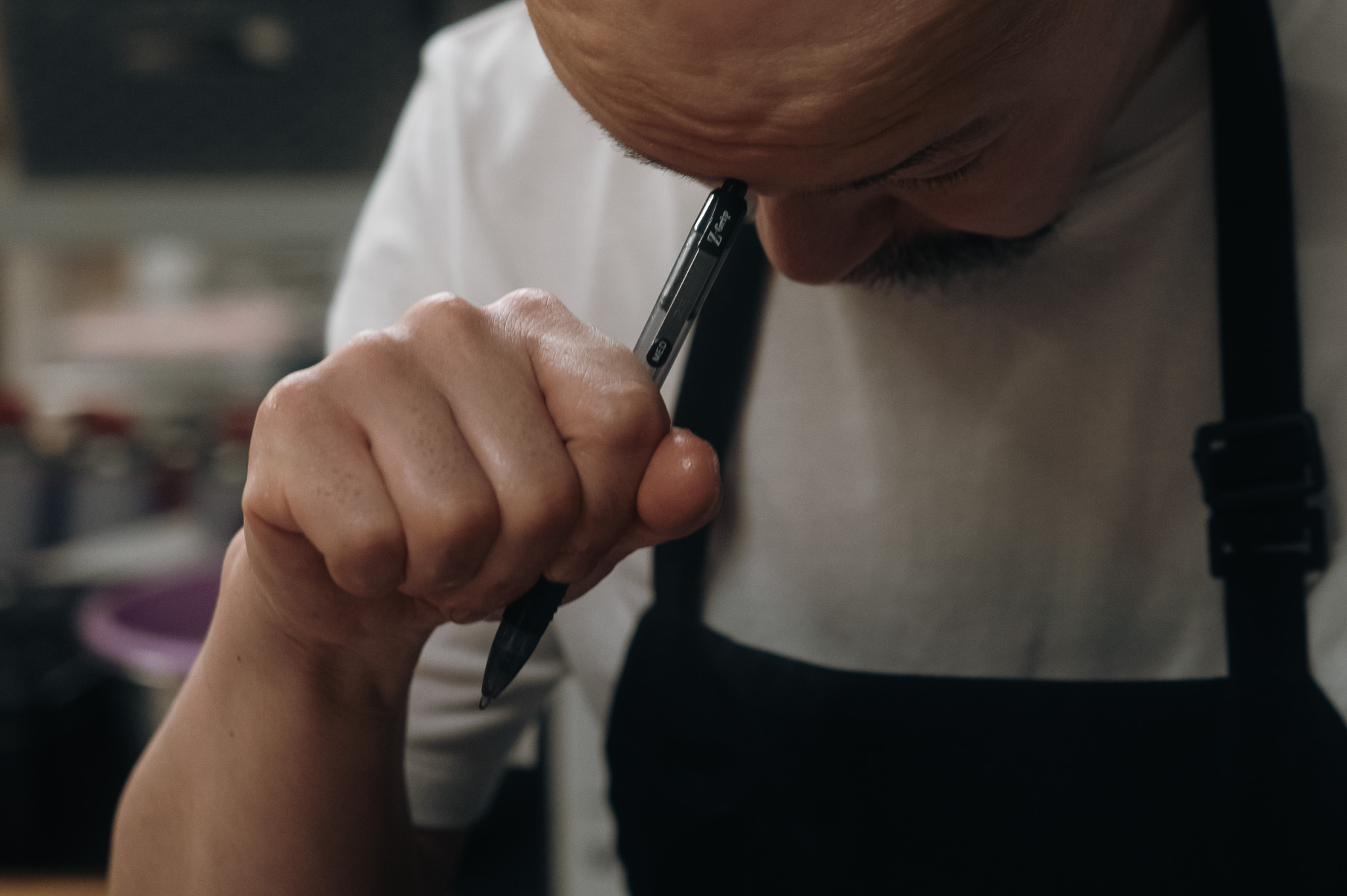 Close-up of the chef thinking, a pen at his lips.